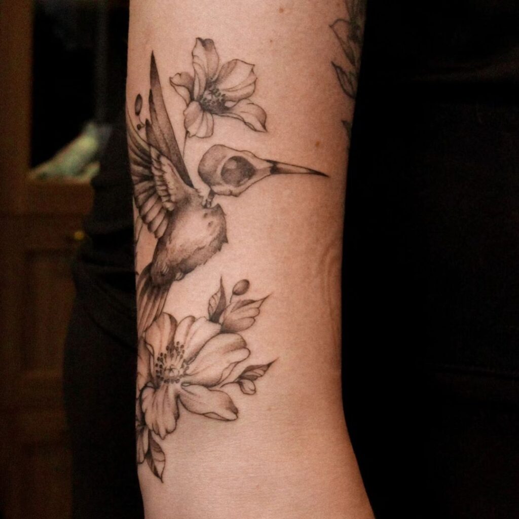 A flesh and skull hummingbird tattoo with flowers