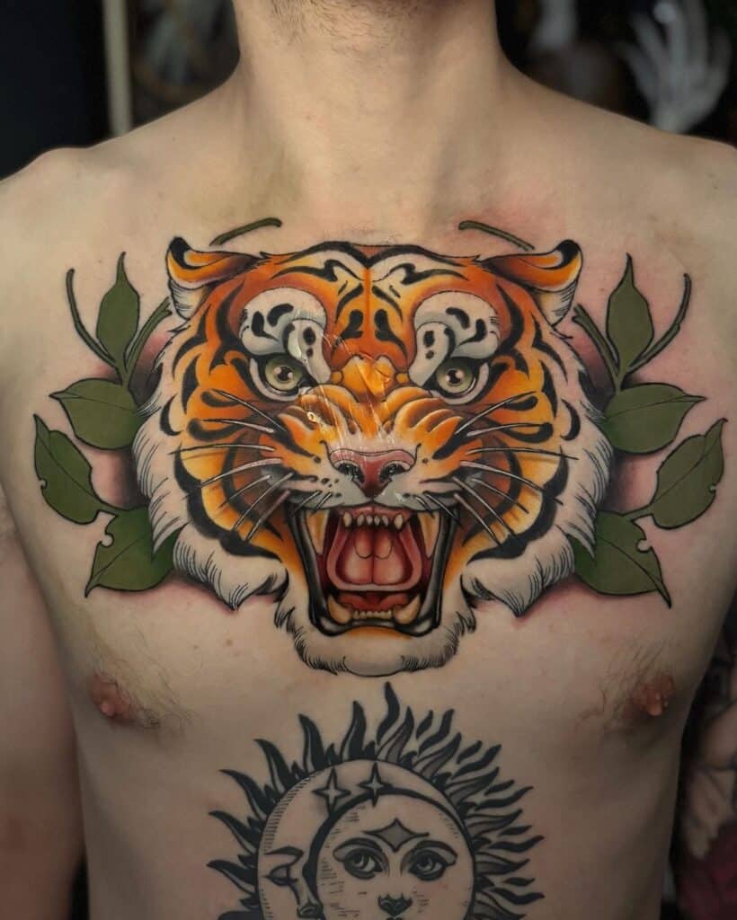 Neo-traditional tattoo on chest featuring a fierce tiger's face with vibrant orange and black stripes, framed by green foliage, displaying bold linework and rich coloration typical of the neo-traditional style.